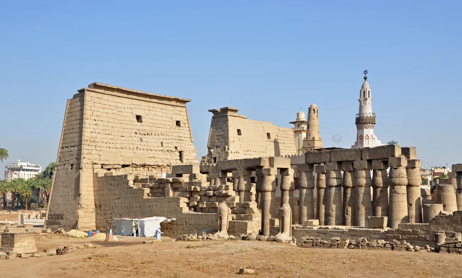 The great pylon of Luxor Temple, fronted by colossal seated statues of Ramesses II and a standing obelisk.