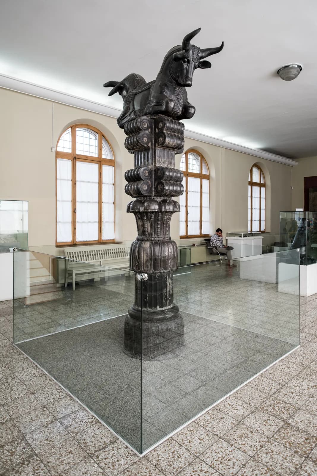 A double-bull (addorsed bull-protome) column capital from the Apadana at Persepolis, now in the National Museum of Iran — two kneeling bulls back to back, the saddle between them carrying the roof beams.