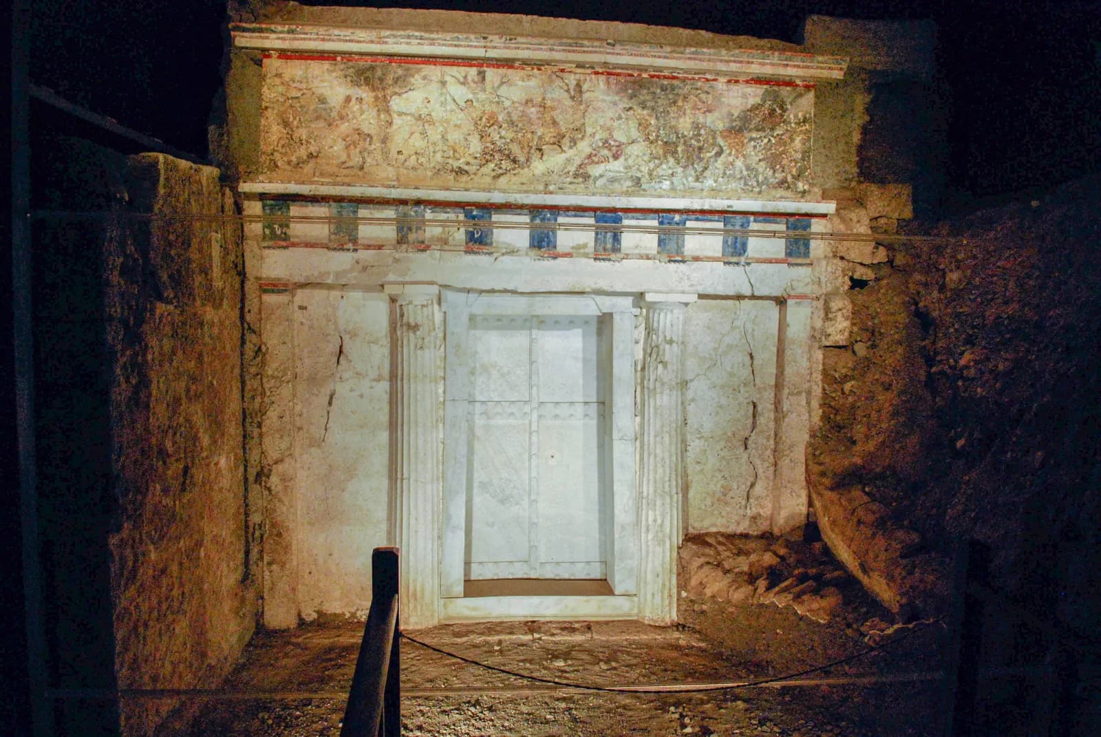 A Doric temple front built into a tomb, with two half-columns, a triglyph frieze and above it a long painted band showing riders and hunters among trees.