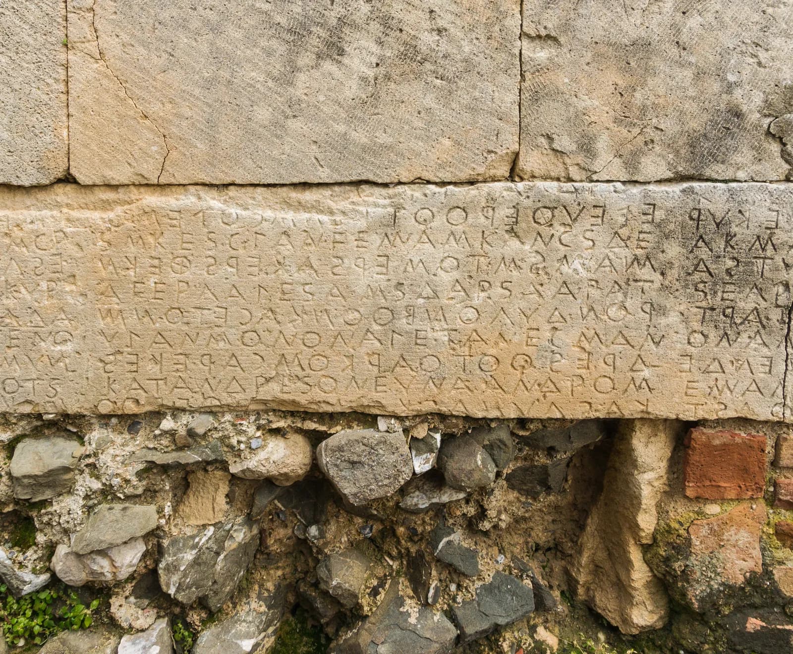 A stretch of the Great Code of Gortyn carved into a curved stone wall — long lines of archaic Greek letters running in boustrophedon, alternately left-to-right and right-to-left.