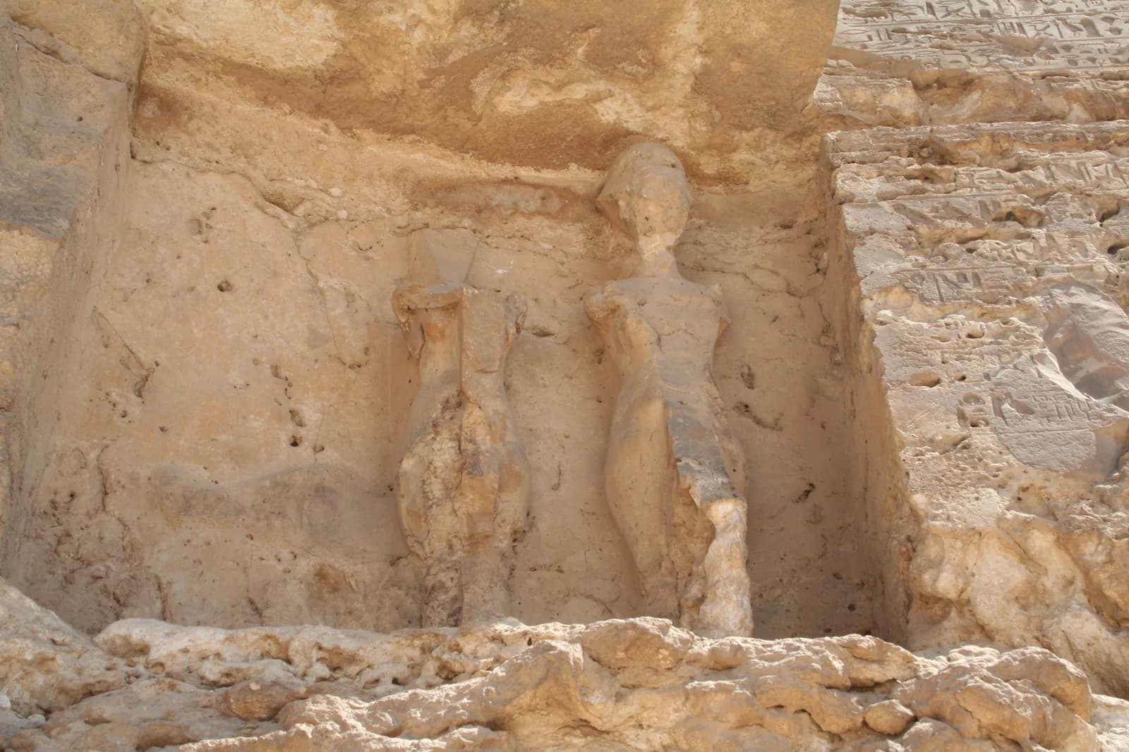 A rock-cut stela in a cliff face, its rounded top carved with the royal family beneath the rayed sun disc, above columns of weathered hieroglyphic text.