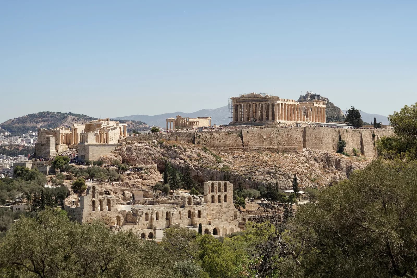 A steep-sided limestone rock rising above a city, carrying a group of ruined marble buildings along its flat summit.