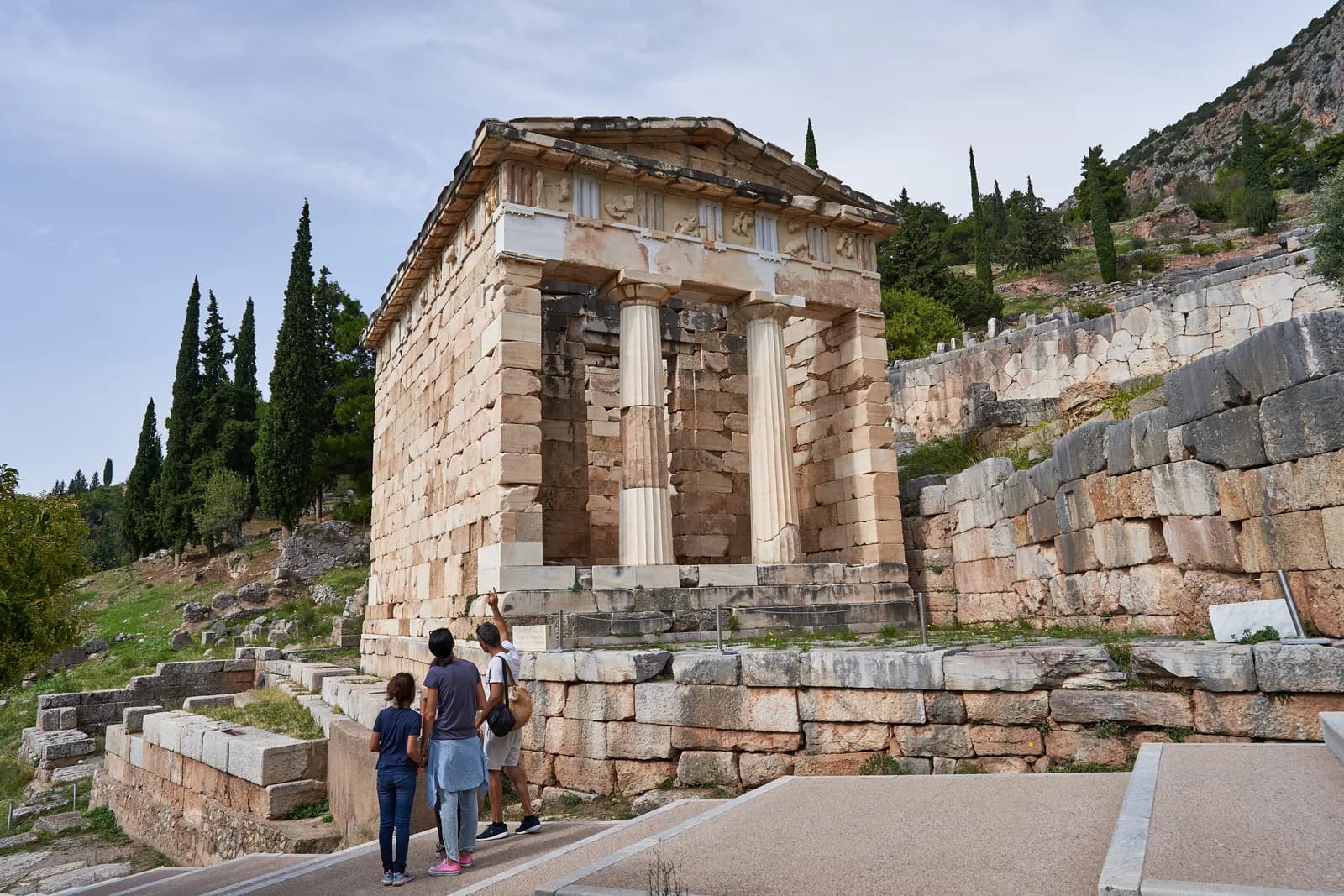 Small marble Doric building standing beside a paved path climbing a terraced hillside.