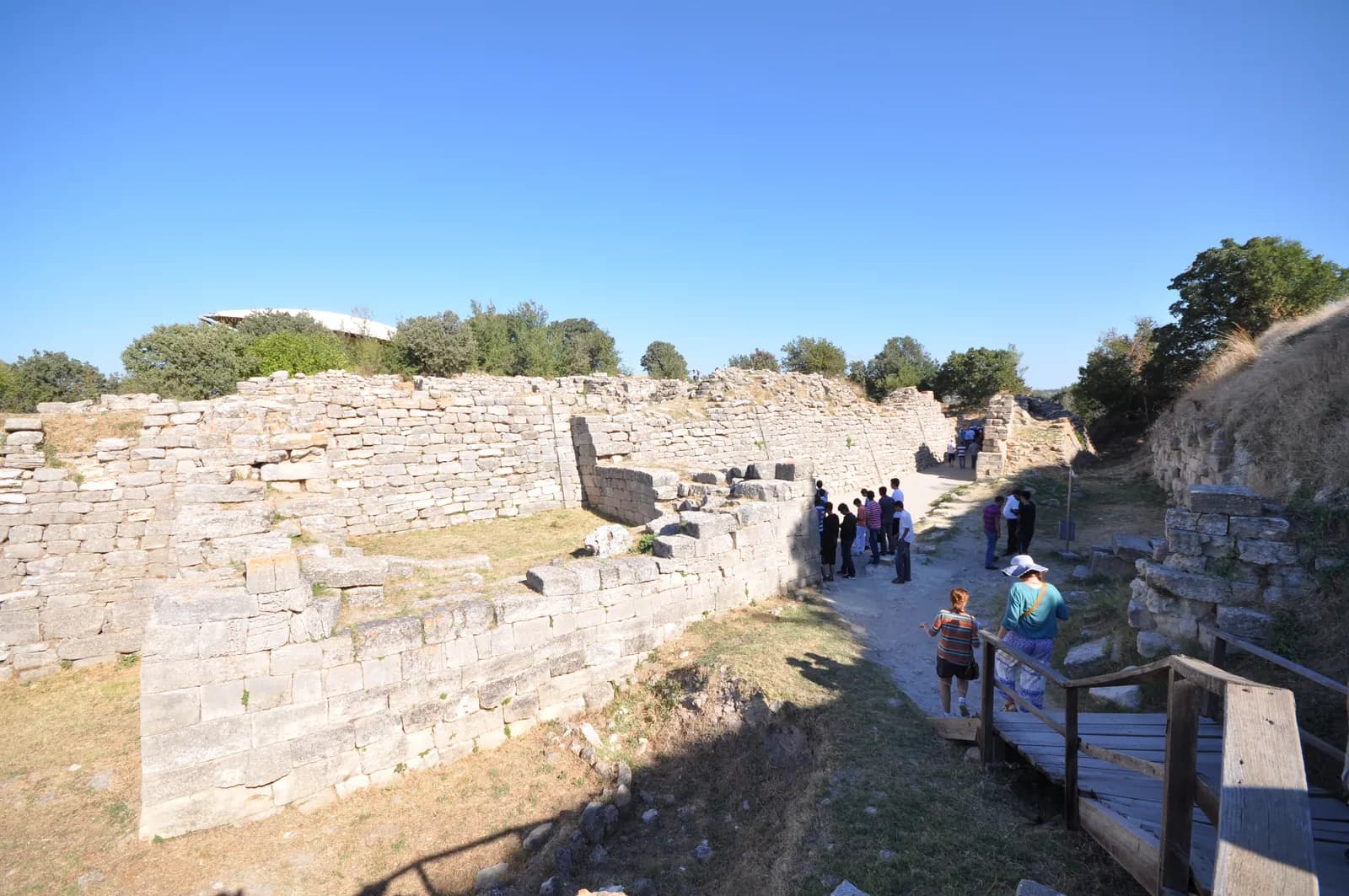 Curving wall of fitted stone blocks with a pronounced inward slope, standing several courses high on a low mound.